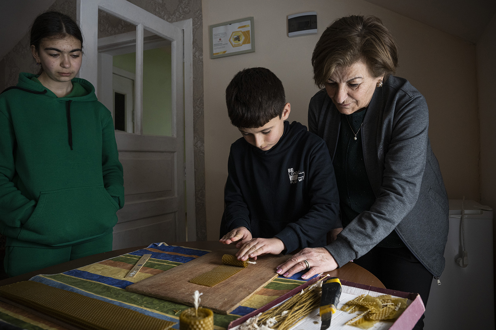une femme montre à deux enfants comment fabriquer des objets à base de cire d'abeille