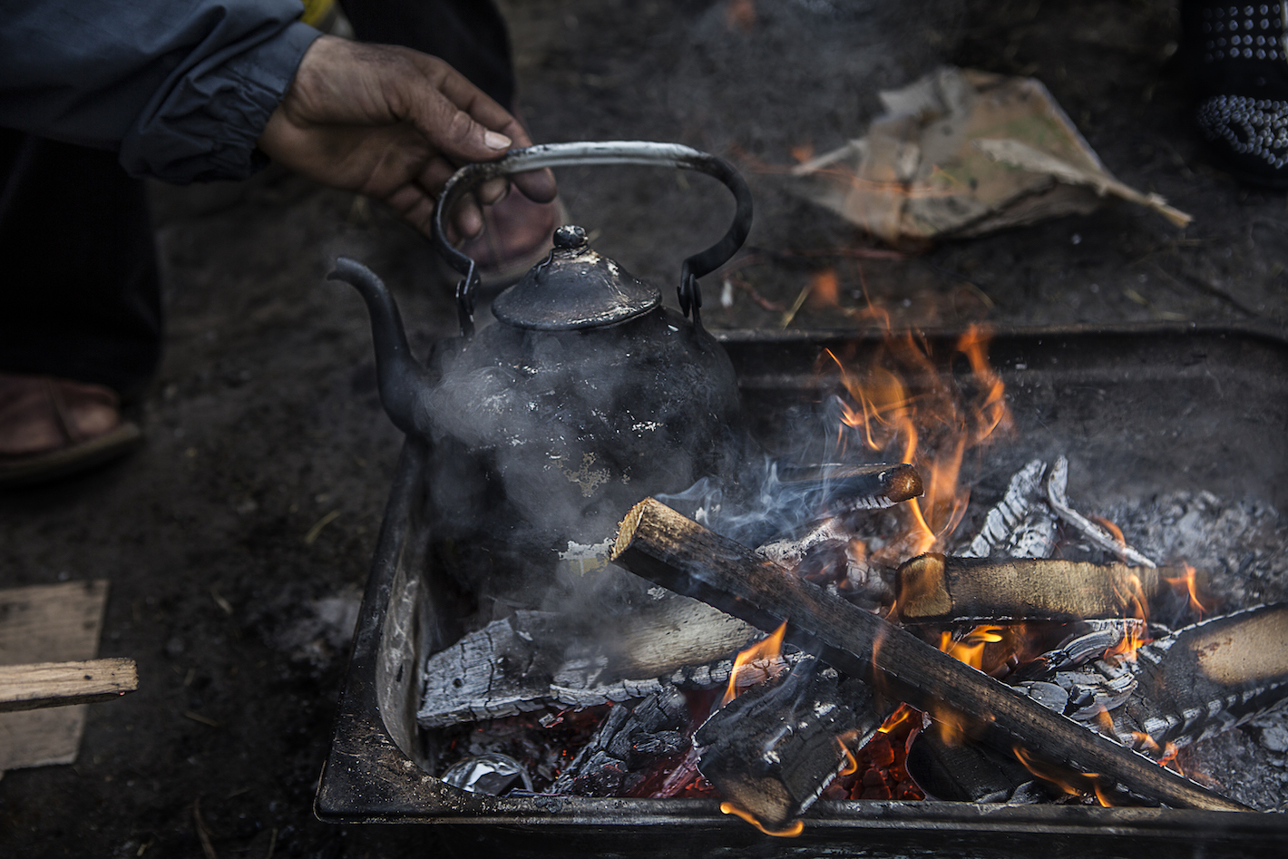 Engoncé dans une veste en cuir, les mains profondément enfoncées dans les poches, Ahmad s’approche du feu de camp autour duquel Mossein, Millad et Parham cherchent à se réchauffer. À leurs pieds, sur les braises fumantes, de l’eau bout dans une théière.