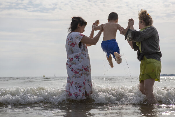 deux femmes jouent dans l'eau avec un enfant et le lèvent au dessus des vagues