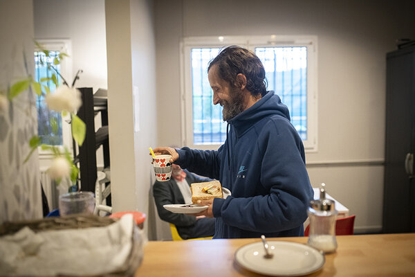 Un homme sourit, un café à la main, à l'accueil de jour de la Voûte.