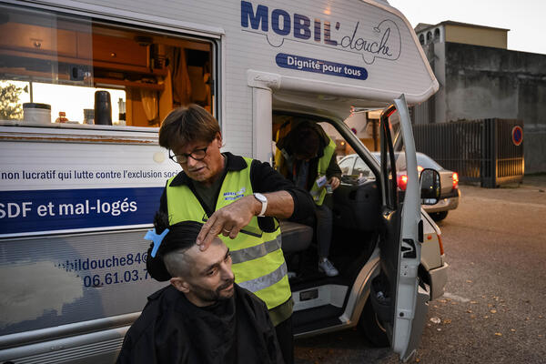 Un bénévole de la douche mobile coupe les cheveux d'un accueilli.