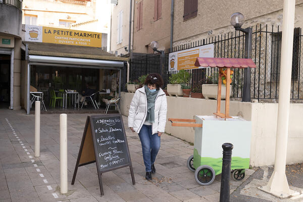 Une bénévole rédige le menu du jour sur l'ardoise, devant la Petite Marmite.