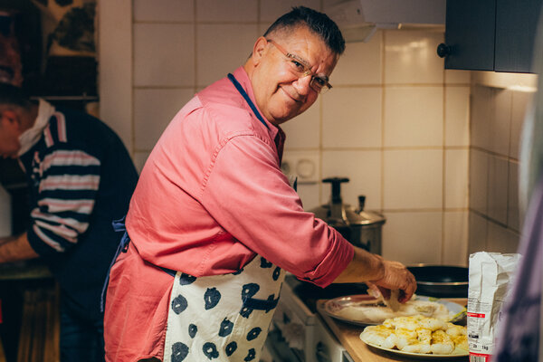 Un homme en tablier de cuisine prépare de la morue panée. Il regarde l’objectif avec un grand sourire. 