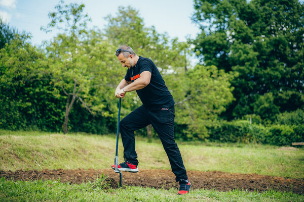 Un homme d’une trentaine d’années laboure un jardin partagé avec une fourche. 