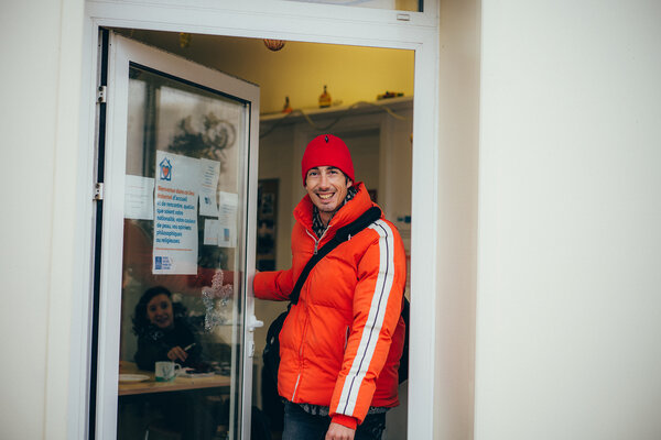 Une jeune homme souriant avec bonnet et doudoune rouge à la porte de la Halte