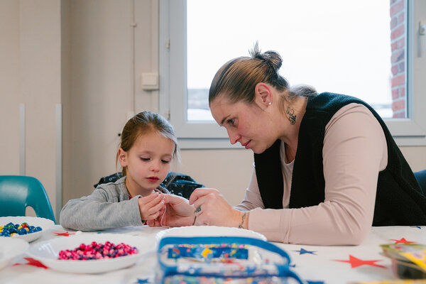 Une mère à côté de sa fille qui confectionne un bracelet en perles